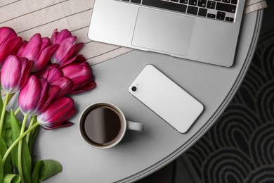 Beautiful tulips, cup of coffee, laptop and smartphone on light gray table indoors, flat lay