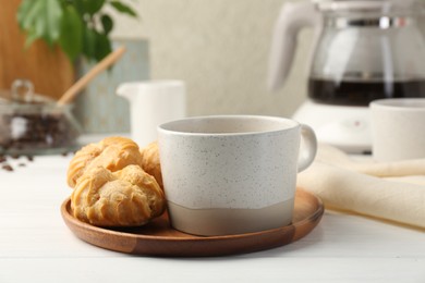 Photo of Cup of drink and tasty profiteroles on white wooden table