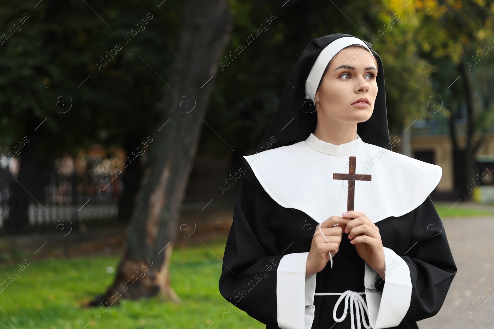 Photo of Young nun with Christian cross in park outdoors, space for text