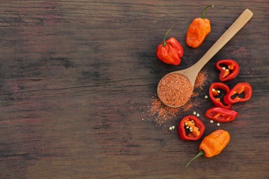 Different ripe chili peppers and spoon with spice on wooden table, flat lay. Space for text