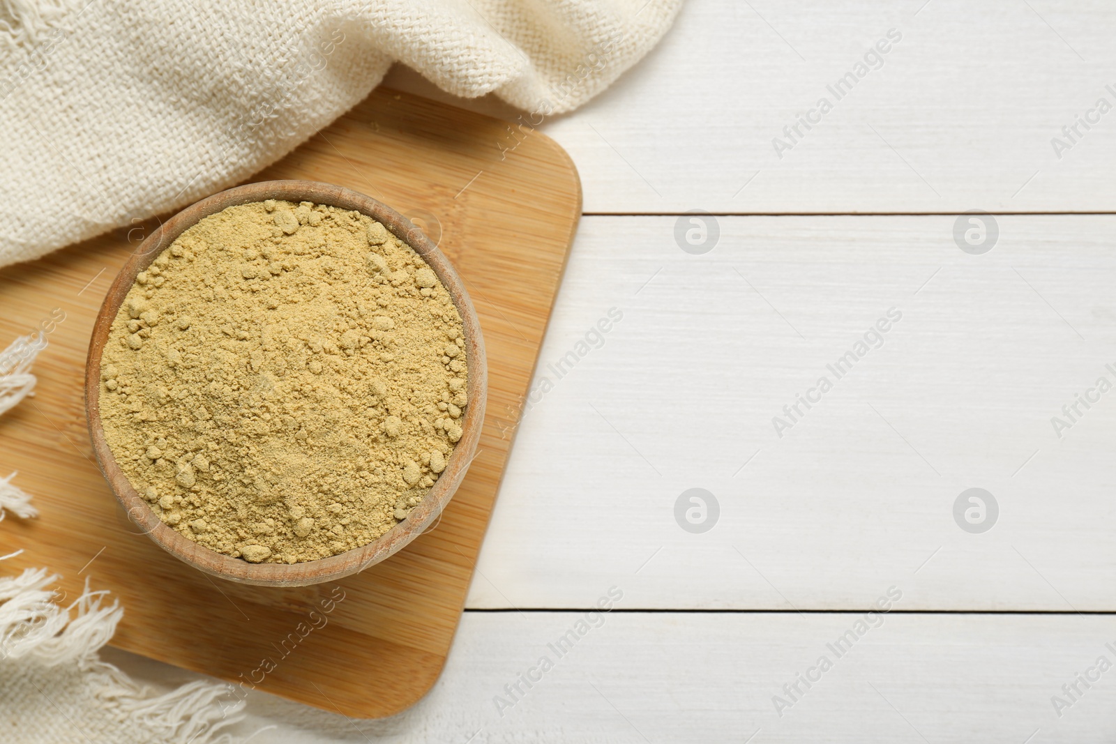 Photo of Bowl of aromatic mustard powder on white wooden table, top view. Space for text