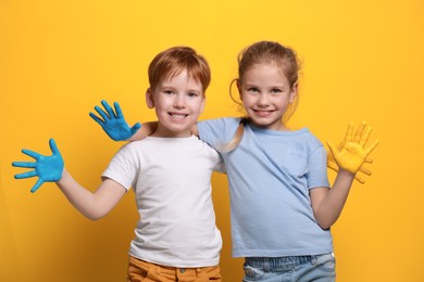 Photo of Little girl and boy with hands painted in Ukrainian flag colors on yellow background. Love Ukraine concept