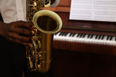 Photo of African-American man playing saxophone indoors, closeup with space for text. Talented musician