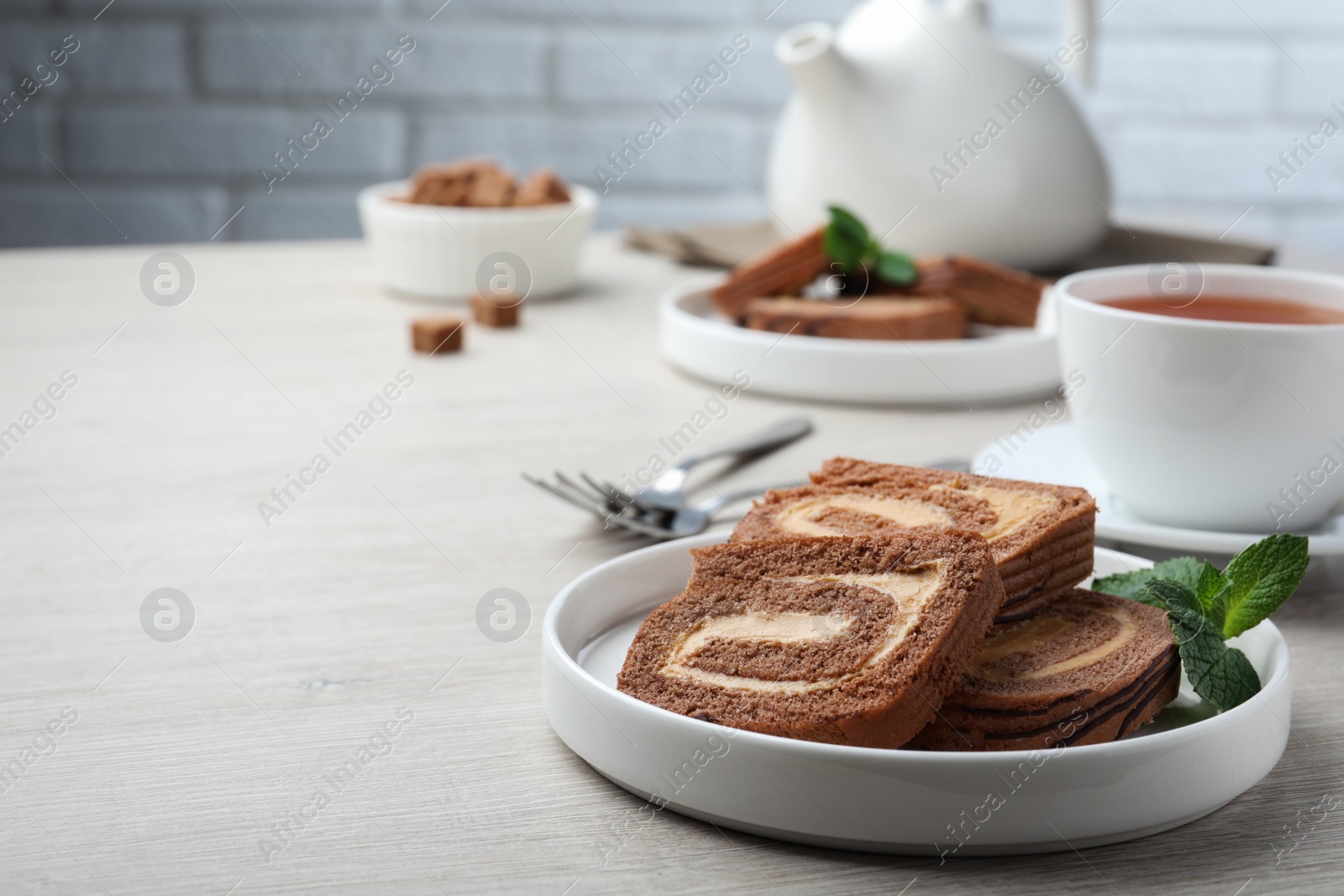 Photo of Tasty chocolate cake roll with cream and mint on light wooden table, space for text