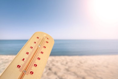 Image of Closeup view of weather thermometer and beautiful seashore on background. Heat stroke warning