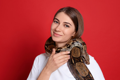 Photo of Young woman with boa constrictor on red background. Exotic pet