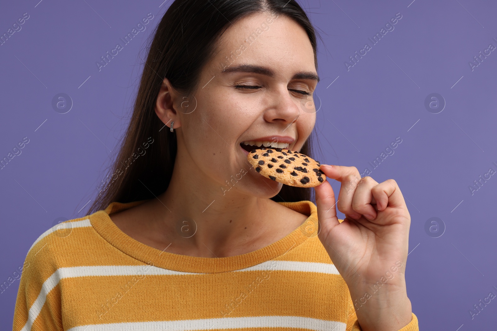 Photo of Young woman with chocolate chip cookie on purple background, closeup