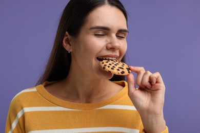 Young woman with chocolate chip cookie on purple background, closeup