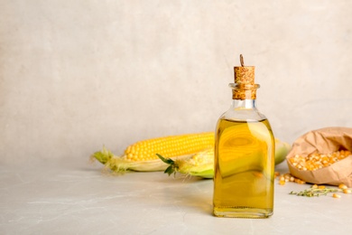 Photo of Bottle of corn oil and fresh cobs on table against light wall