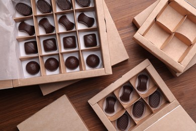 Photo of Many delicious chocolate candies in boxes on wooden table, flat lay. Production line