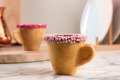 Photo of Delicious edible biscuit cup decorated with sprinkles on white marble table