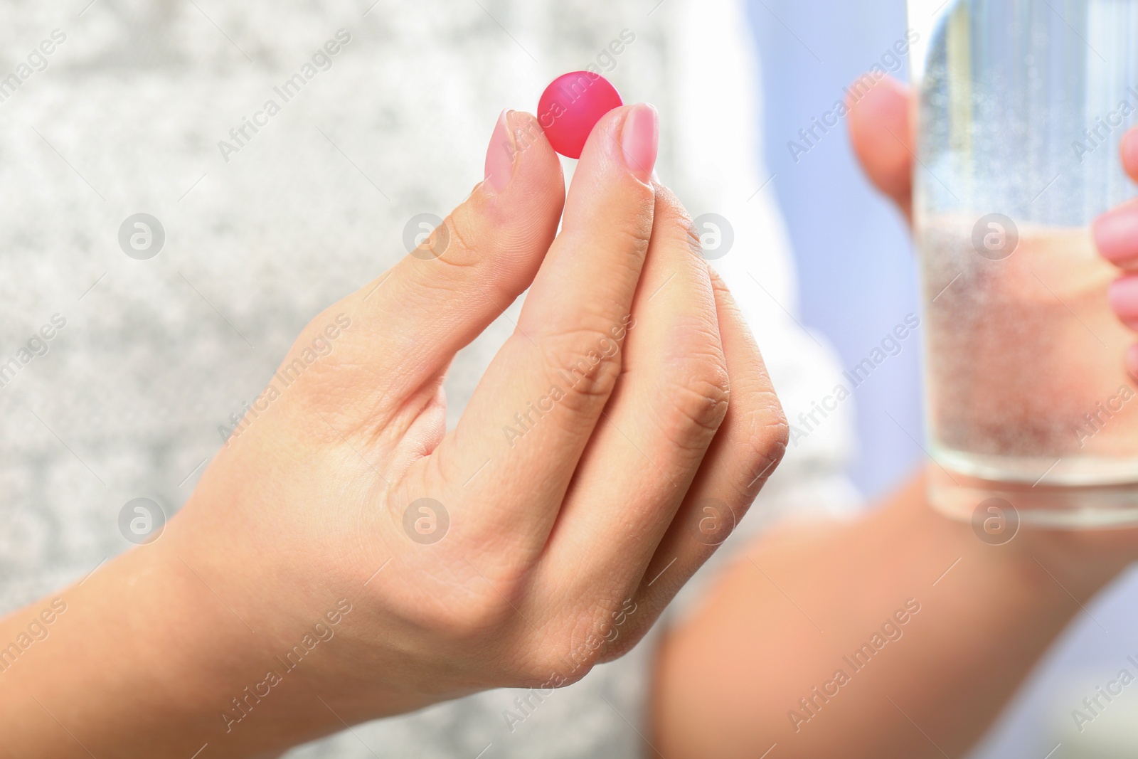 Photo of Woman holding pill and glass of water on blurred background, closeup