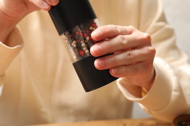 Woman grinding pepper with shaker at table, closeup