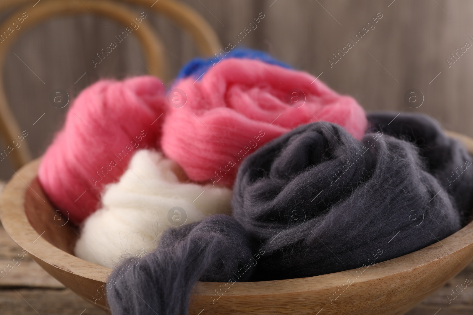 Photo of Colorful felting wool in bowl on table, closeup