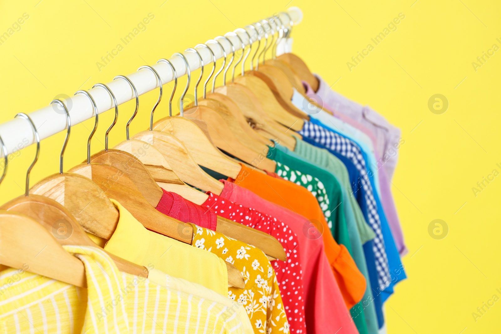 Photo of Bright clothes hanging on rack against yellow background, closeup. Rainbow colors