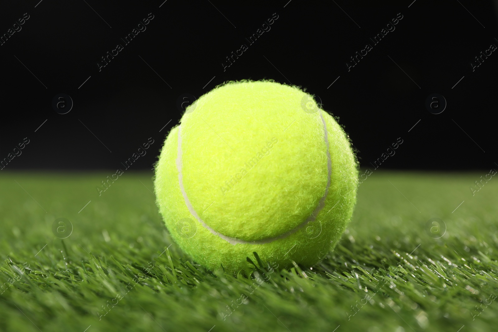 Photo of Tennis ball on green grass against black background, closeup