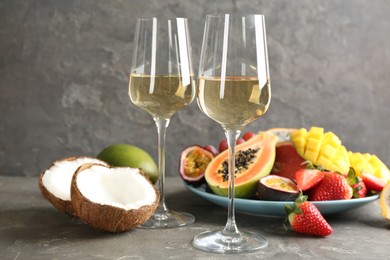 Delicious exotic fruits and glasses of wine on grey table