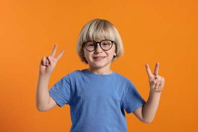 Photo of Cute little boy wearing glasses on orange background