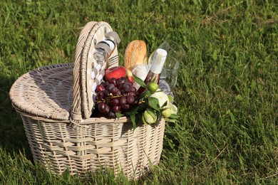 Photo of Picnic basket with tasty food, flowers and cider on grass. Space for text