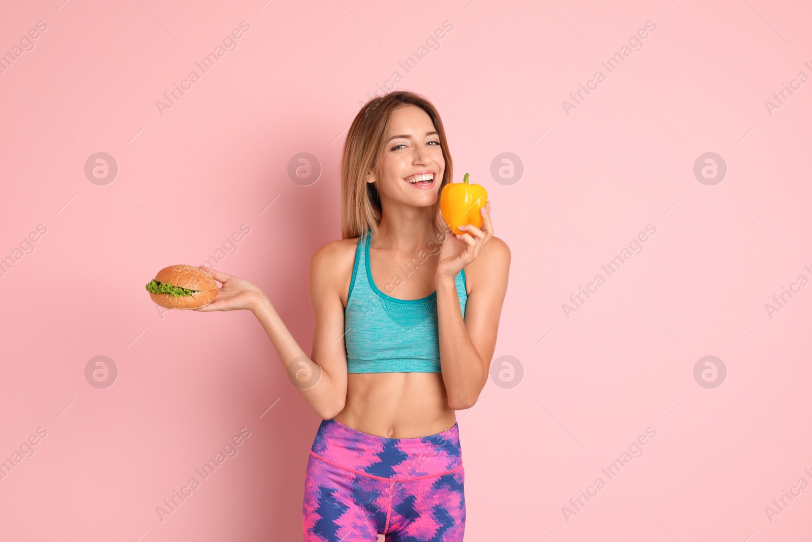 Photo of Young woman with burger and bell pepper on color background. Choice between diet and unhealthy food