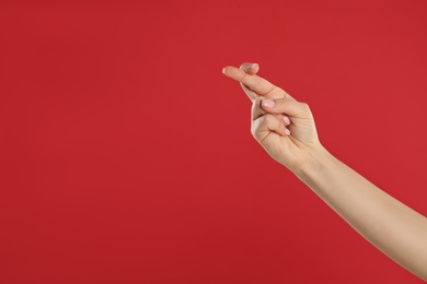 Photo of Woman holding fingers crossed on red background, closeup with space for text. Good luck superstition