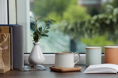 Photo of Cup of coffee with books and home decor on wooden window sill