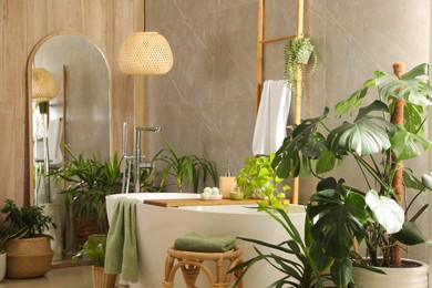 Modern white tub and beautiful green houseplants in bathroom. Interior design