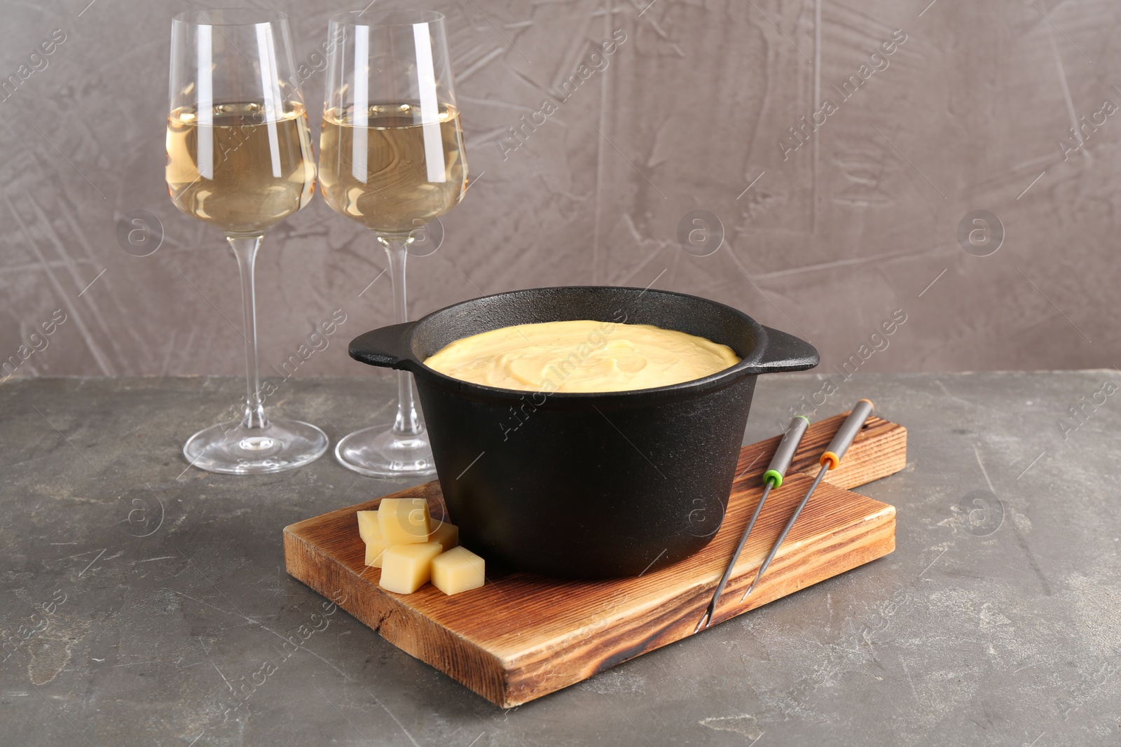 Photo of Fondue pot with tasty melted cheese, forks and wine on grey table