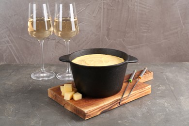 Fondue pot with tasty melted cheese, forks and wine on grey table