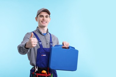 Photo of Professional repairman with tool box showing thumbs up on light blue background. Space for text