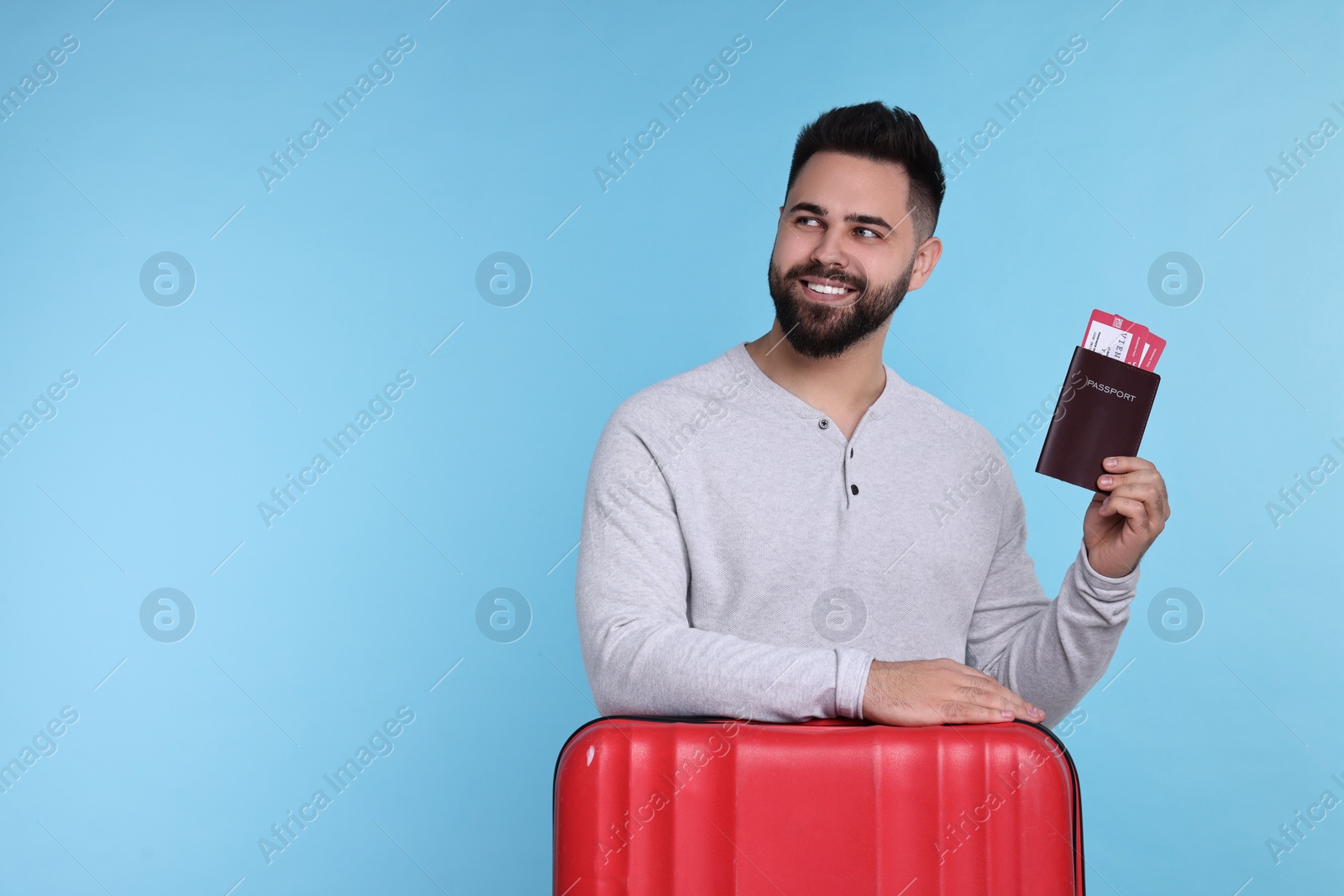 Photo of Smiling man with passport, tickets and suitcase on light blue background. Space for text
