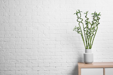 Vase with green bamboo on table against brick wall. Space for text