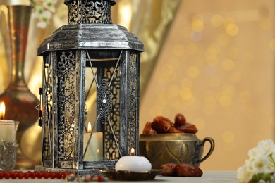Arabic lantern, burning candles, dates and misbaha on table against blurred lights