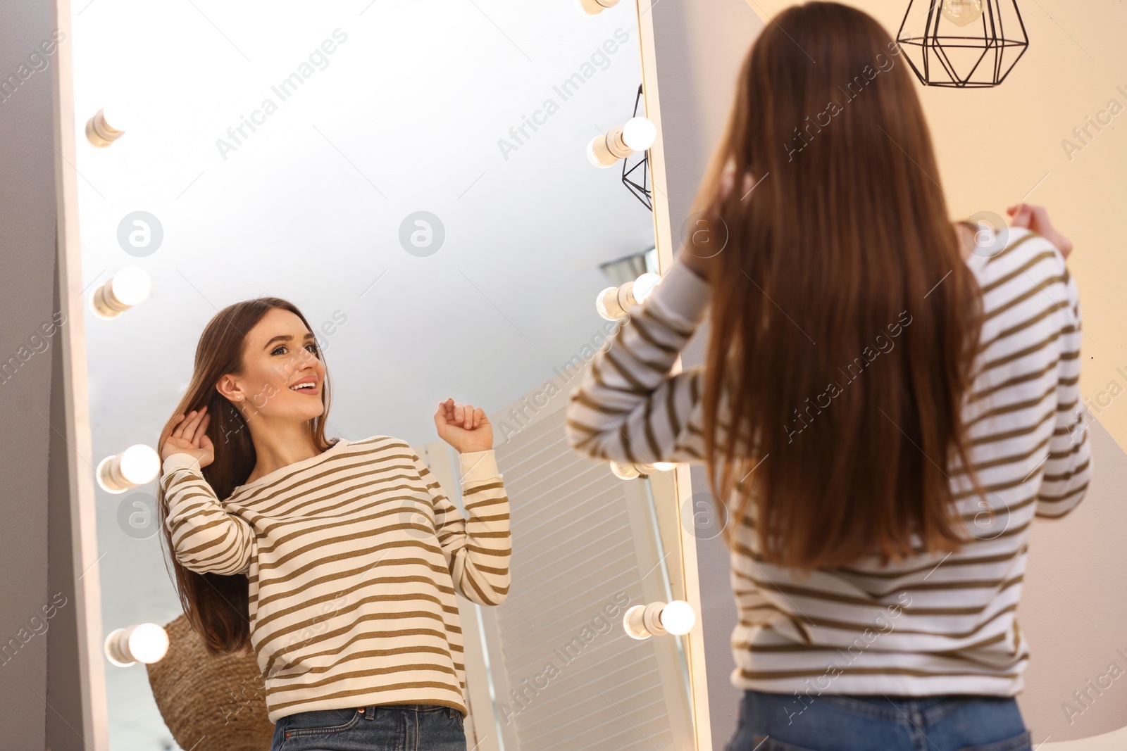 Photo of Beautiful young woman looking at herself in large mirror indoors