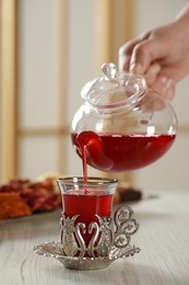 Photo of Woman pouring tasty Turkish tea into glass in vintage holder at white wooden table, closeup