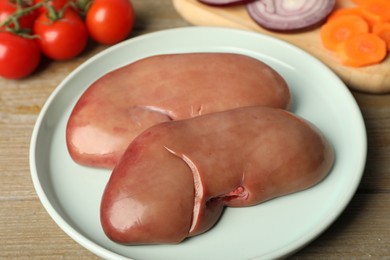 Photo of Plate with fresh raw pork kidneys on wooden table, closeup