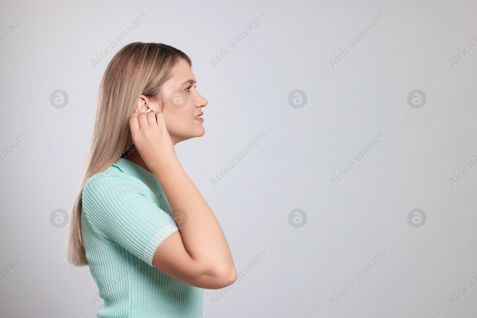 Photo of Young woman cleaning ear with cotton swab on light grey background. Space for text