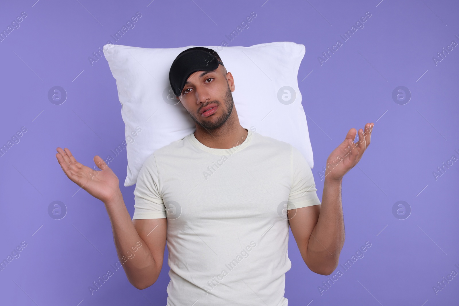 Photo of Tired man with pillow and sleep mask on violet background. Insomnia problem