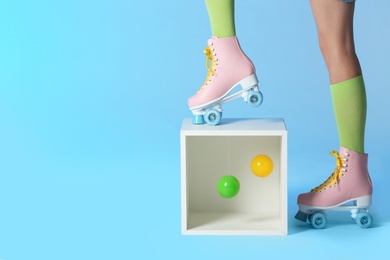 Photo of Woman wearing vintage roller skates near storage cube with balls on color background, closeup. Space for text