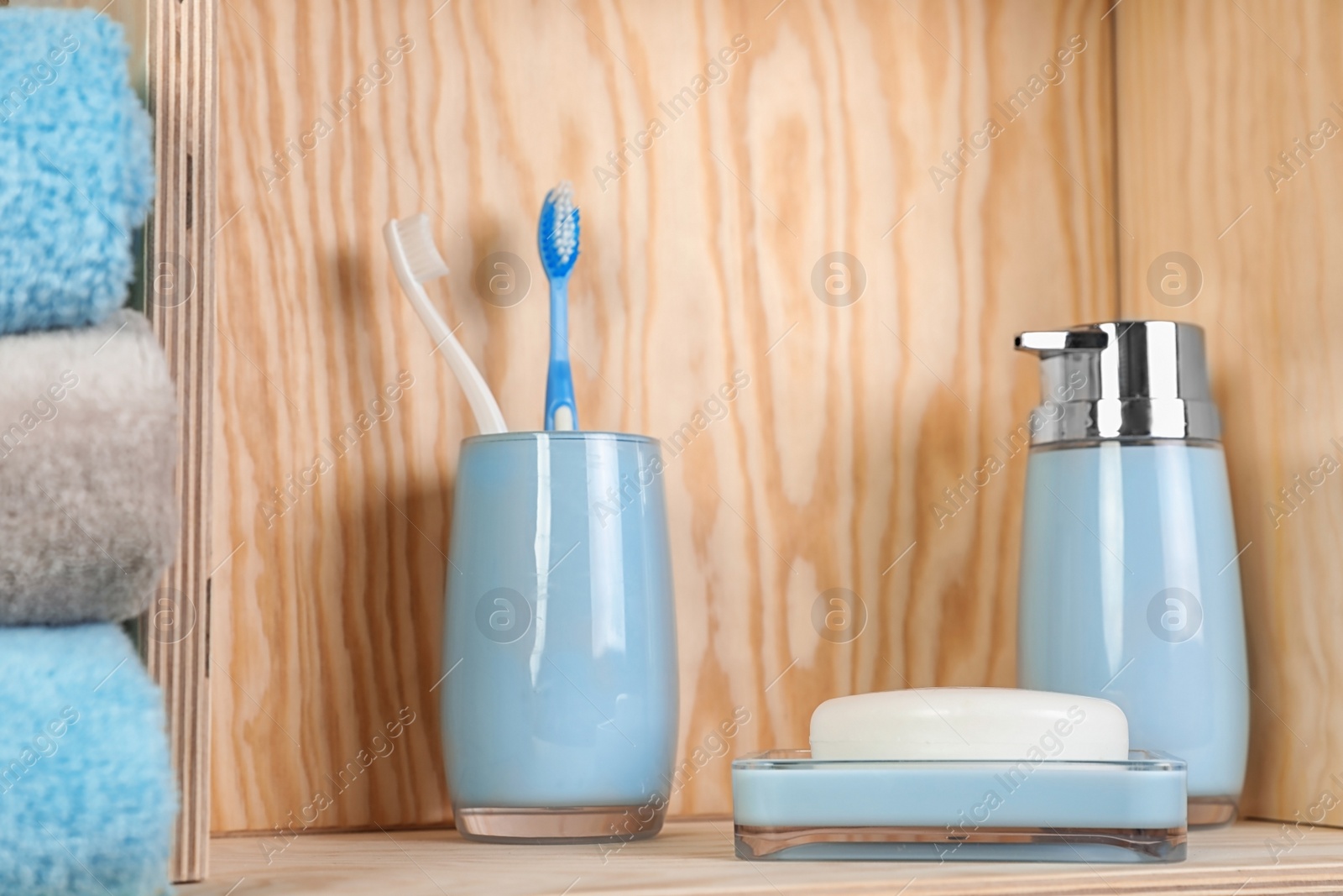 Photo of Dish with soap, bottle of shampoo and toothbrushes on wooden shelf