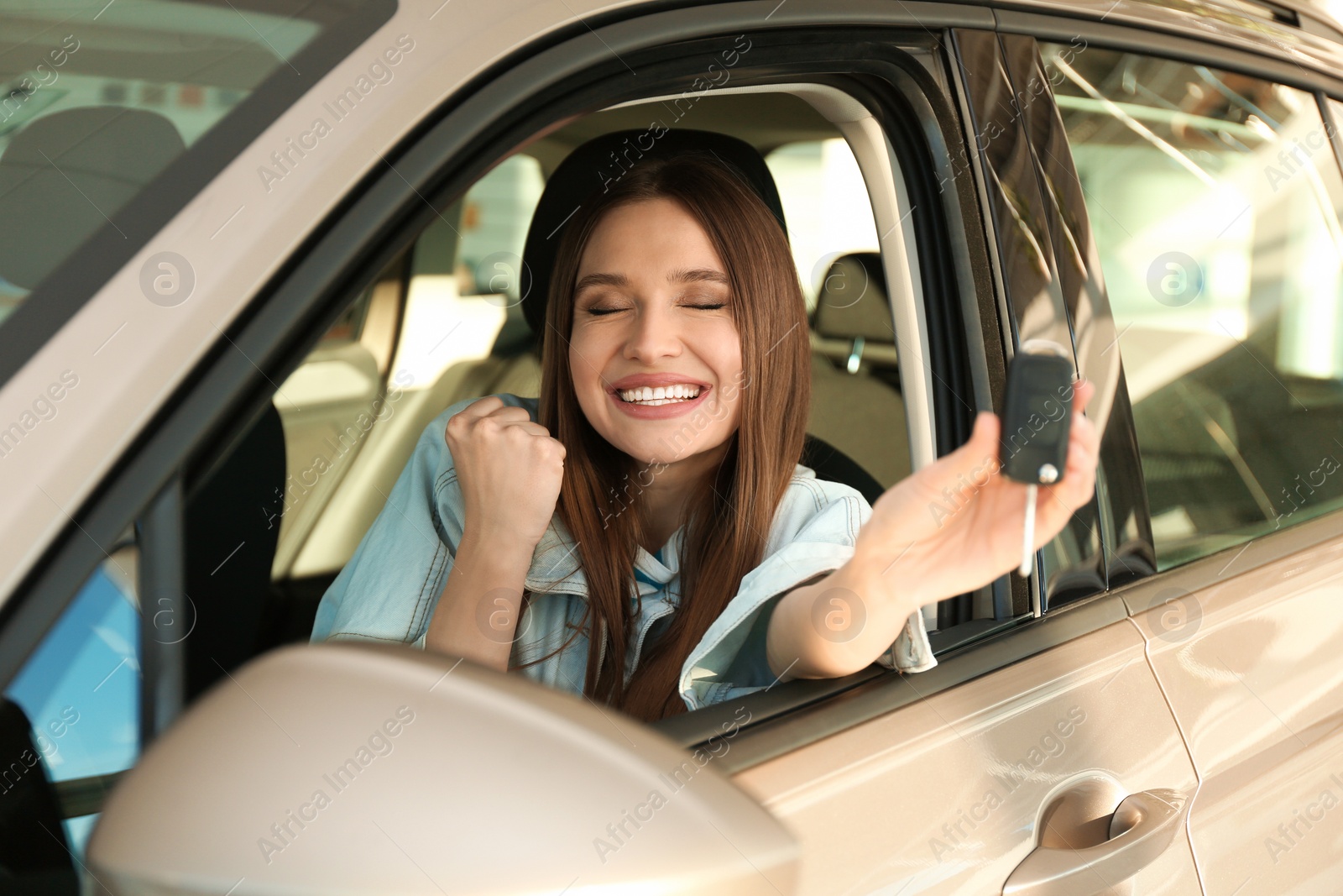 Photo of Beautiful woman with car key sitting in modern auto at dealership