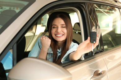 Beautiful woman with car key sitting in modern auto at dealership