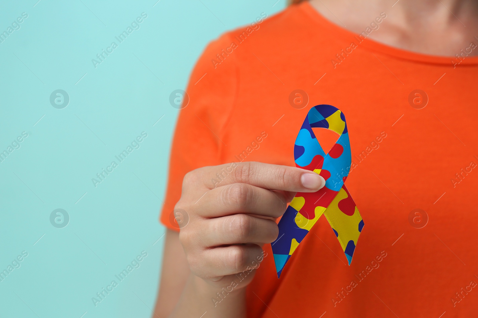 Image of World Autism Awareness Day. Woman with colorful puzzle ribbon on light blue background, closeup