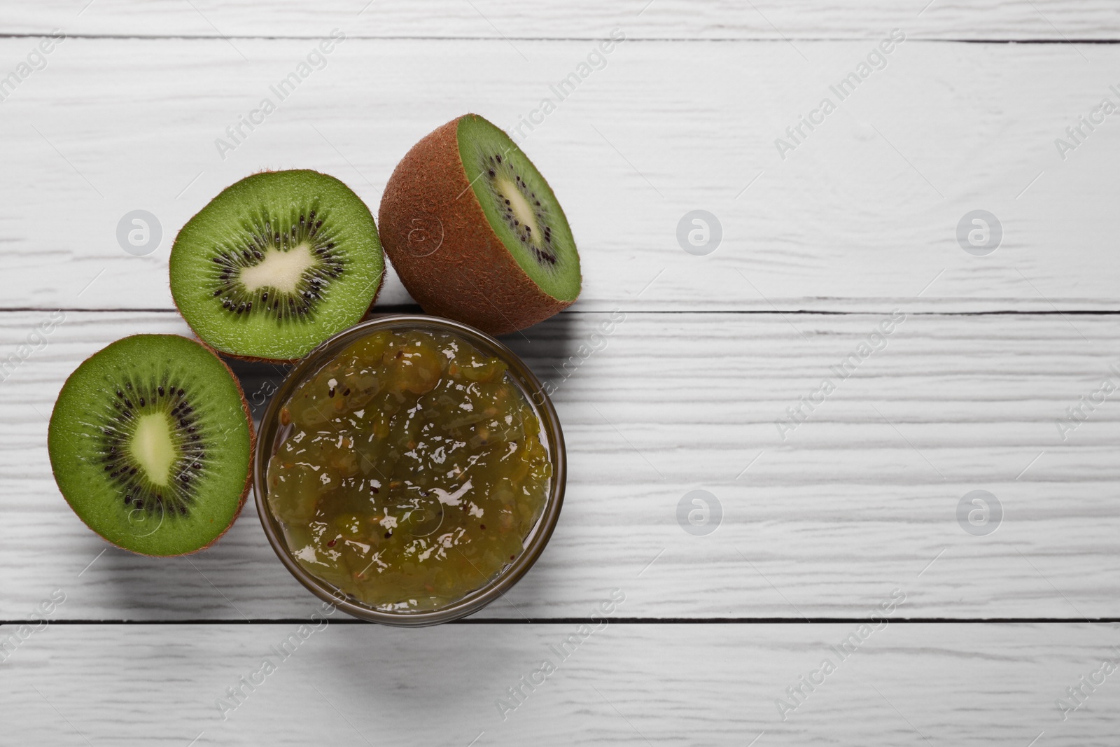 Photo of Jar with delicious kiwi jam and fresh fruits on white wooden table, flat lay. Space for text