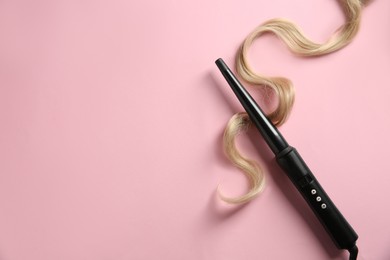 Photo of Modern clipless curling iron and blonde hair lock on pink background, top view. Space for text