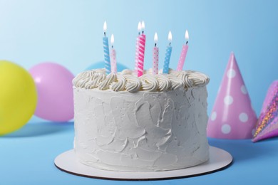 Photo of Delicious cake with burning candles and festive decor on light blue background