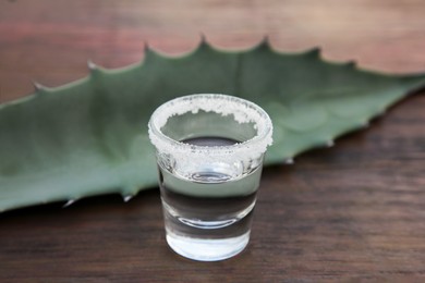 Photo of Mexican tequila shot with salt and green leaf on wooden table, closeup. Drink made of agava
