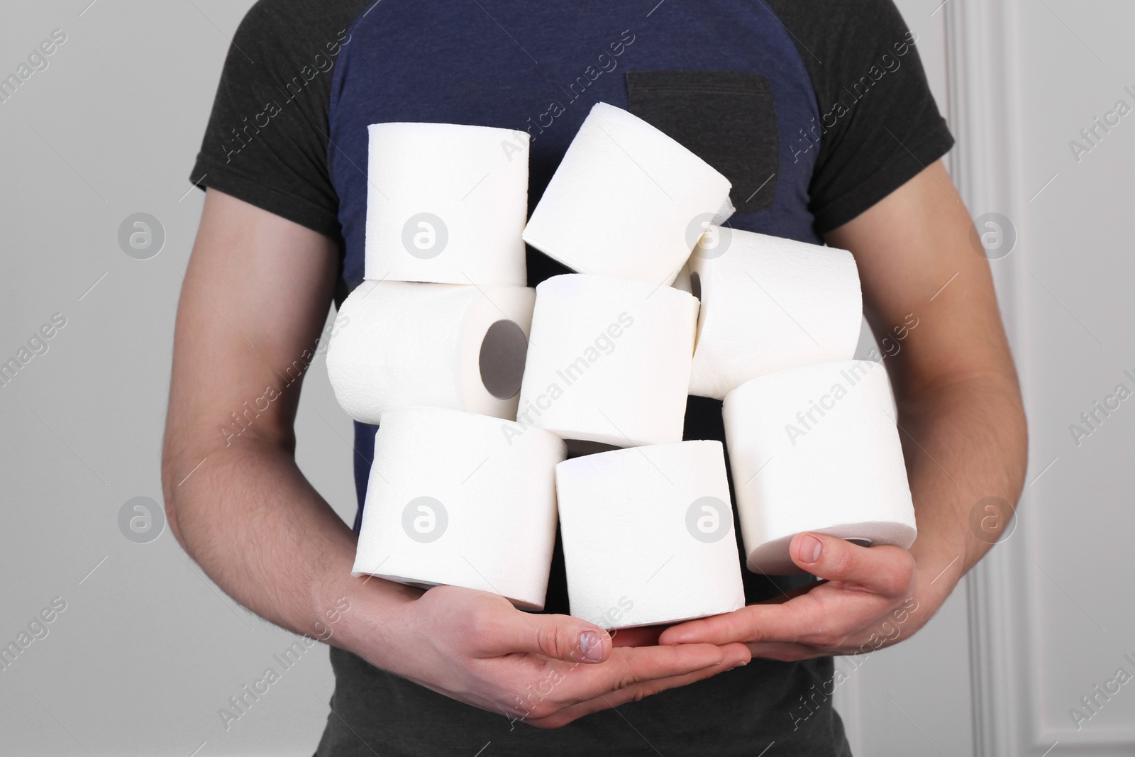 Photo of Man with many toilet paper rolls near white wall, closeup