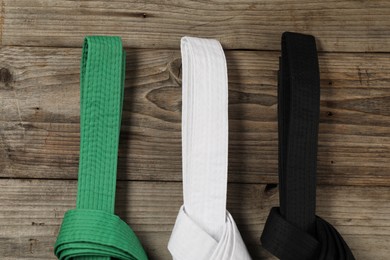 Photo of Colorful karate belts on wooden background, flat lay