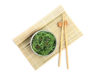Photo of Japanese seaweed salad in bowl with chopsticks  and wicker mat on white background, top view